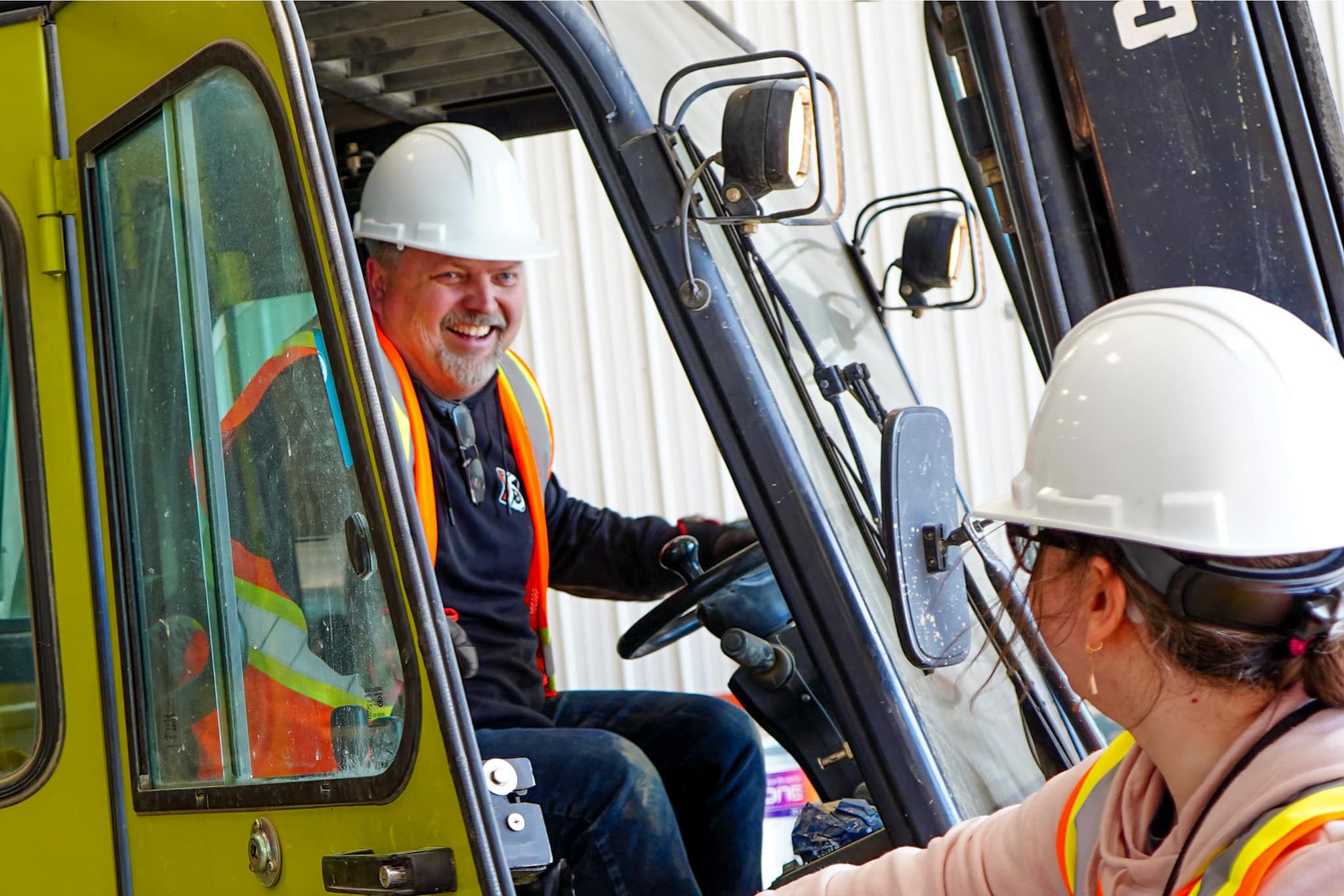 A worker in PPE gear is smiling in the forklift